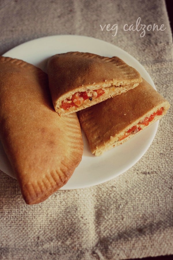 a whole calzone and a halved calzone served on a white plate with text layover.