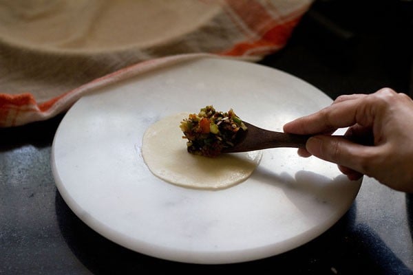 placing vegetable stuffing with a wooden spoon in the center of the rolled dough