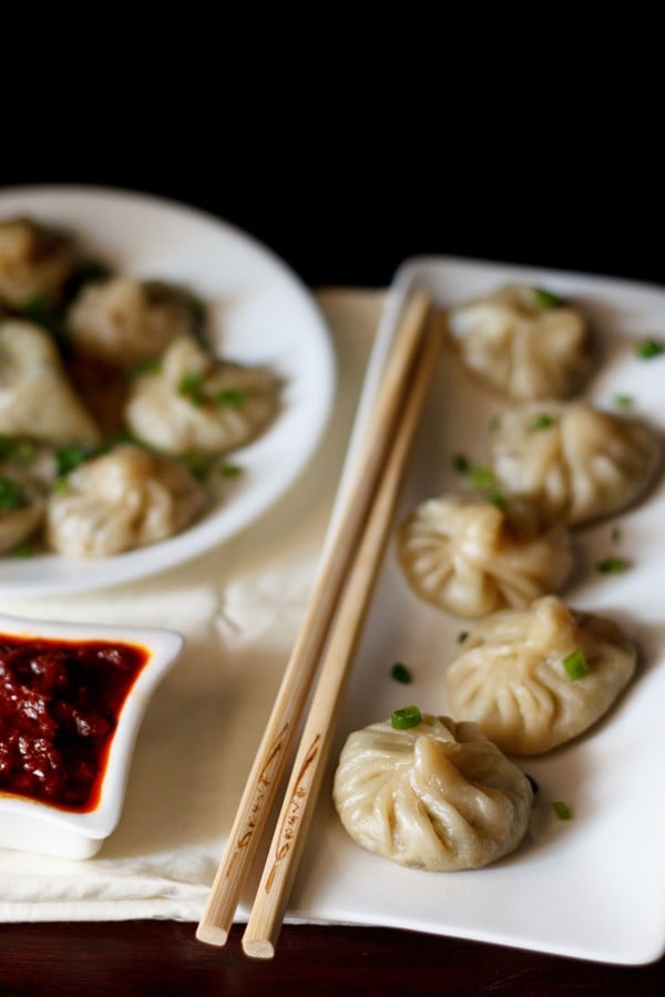 Veg momos arranged on a white rectangular long tray with a bamboo chopsticks by the side