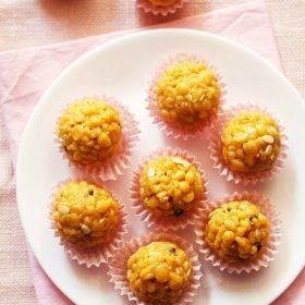 overhead shot of 6 boondi laddu in pink muffin liners on a white plate placed on pink napkin with text layovers.