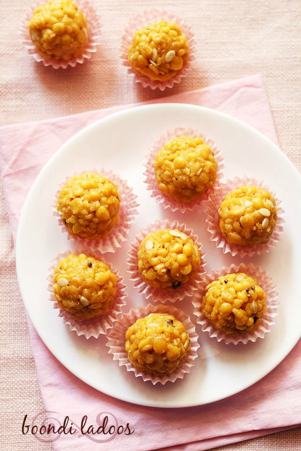 overhead shot of 6 boondi laddu in pink muffin liners on a white plate placed on pink napkin with text layovers.