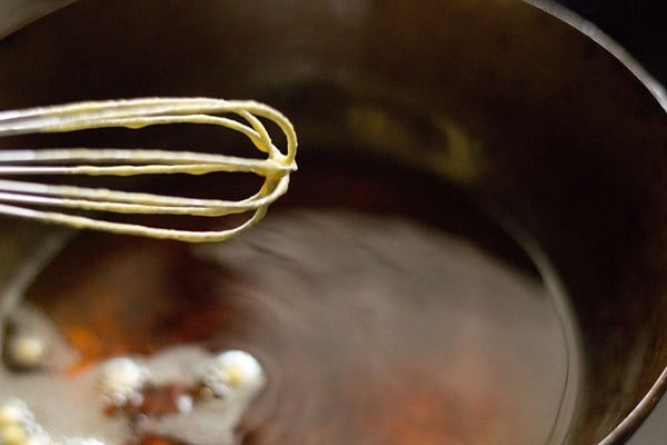 whisk with batter droplets falling in a wok filled with hot oil