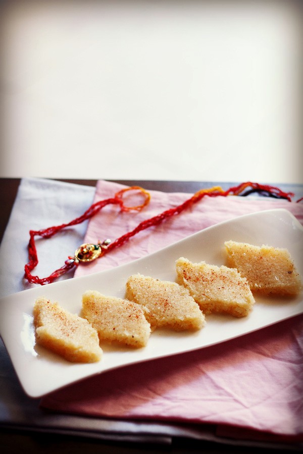 coconut burfi slices on a white platter with a rakhi in the bacakground.