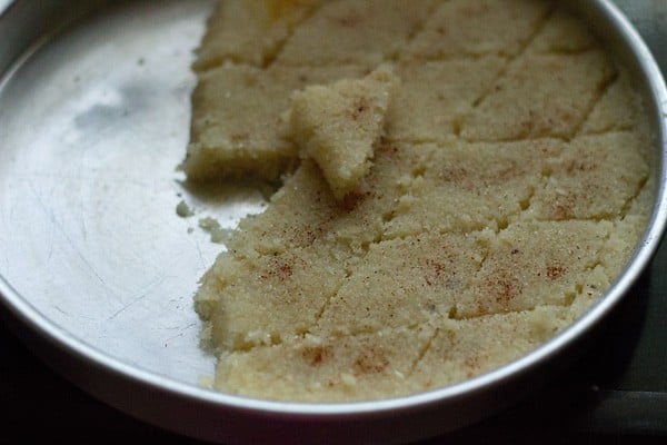 sliced coconut barfi kept on top of coconut burfi in round baking tray.