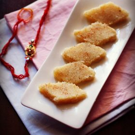 coconut burfi slices on a white platter with a rakhi in the background.