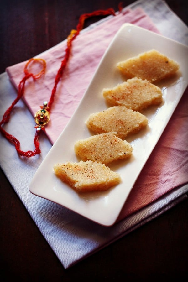 coconut burfi slices on a white platter with a rakhi in the background.