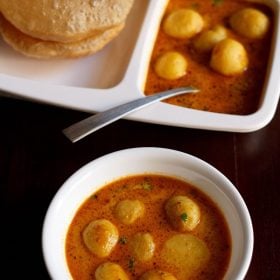 dum aloo banarasi served in a bowl and a plate with pooris and a spoon in it.