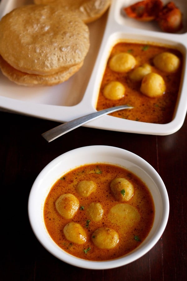 dum aloo banarasi served in a bowl and a plate with pooris and a spoon in it.