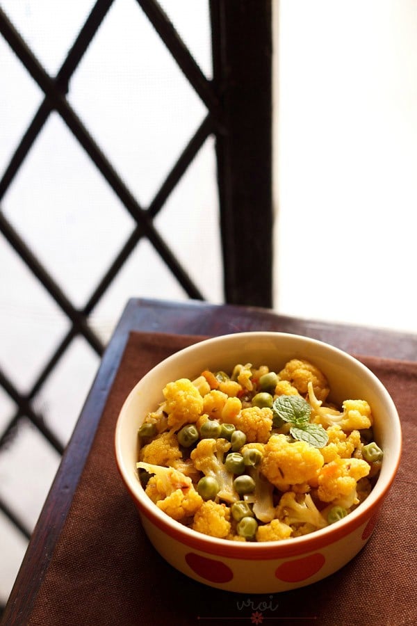 gobi matar garnished with mint leaves and served in a dotted ceramic bowl. 