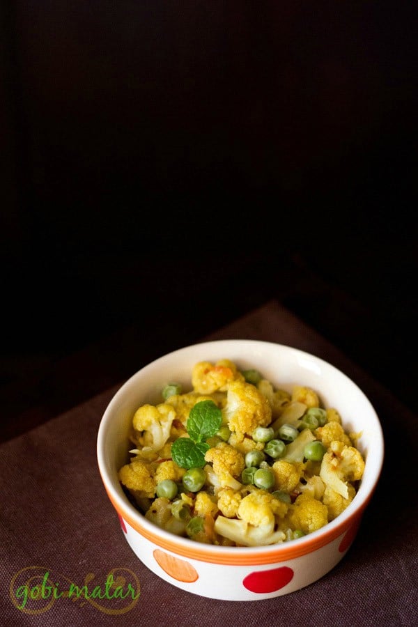 gobi matar garnished with mint leaves and served in a dotted ceramic bowl with text layover.