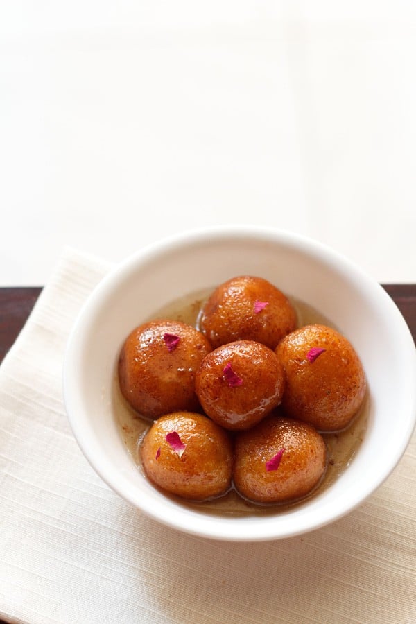 gulab jamun served in a white bowl on a white napkin