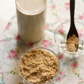 milk masala powder in a bowl, in a spoon kept in a bowl and a glass of masala milk in the background.