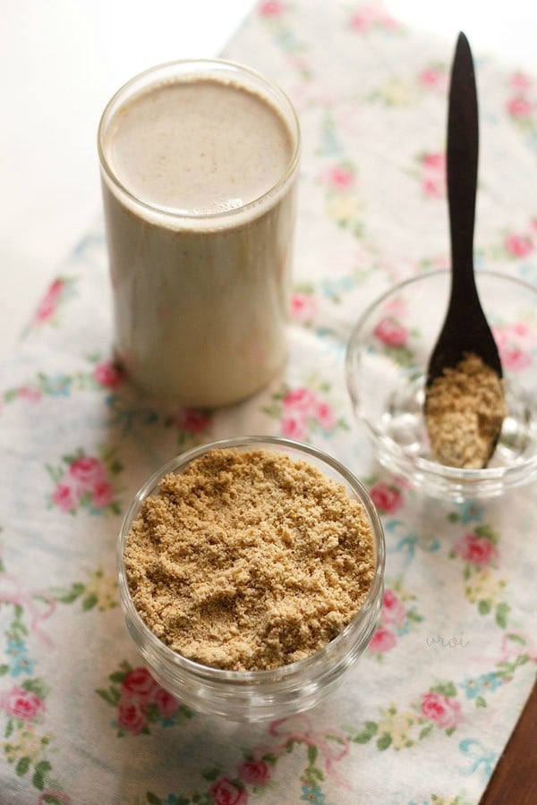 milk masala powder in a bowl, in a spoon kept in a bowl and a glass of masala milk in the background.