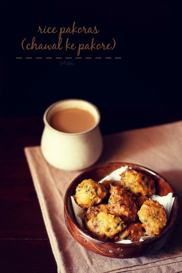 rice pakora served on a wooden plate with a mug of tea kept on the left side and text layovers.