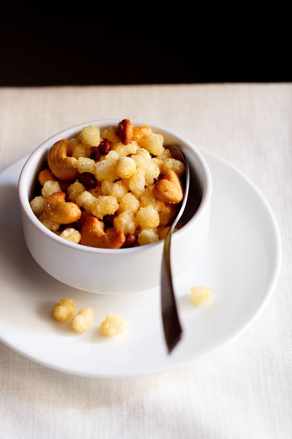 Sabudana Chivda is served in a white bowl with a spoon inside and served on a white plate.