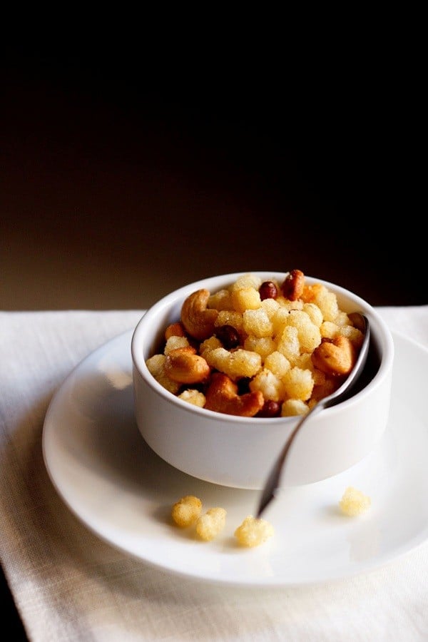 sabudana chivda served in a white bowl with a spoon in it and kept on a white plate. 