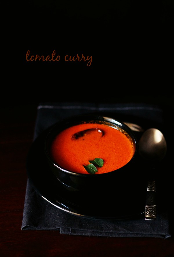 tomato curry garnished with curry leaves and served in a black bowl kept on a black plate with a spoon kept on right side of the bowl and text layover. 