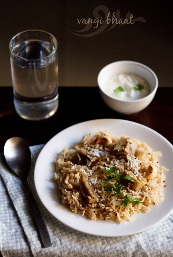 maharashtrian vangi bath served on a white plate with a spoon kept on the left side, a glass of water above that, a bowl of curd on the top right side and text layover. 