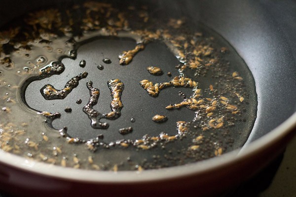 mustard seeds and cumin seeds spluttering in hot peanut oil in pan. 