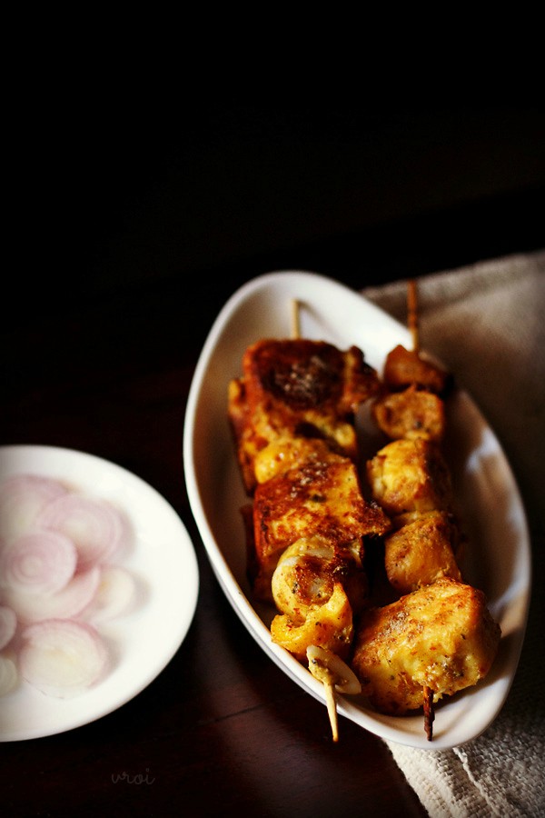 achari paneer tikka served in a white plate with onions