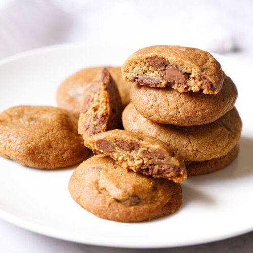 eggless chocolate chip cookies stacked and kept randomly on a white plate