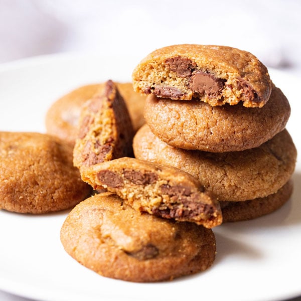 eggless chocolate chip cookies stacked, broken and kept randomly on a white plate.