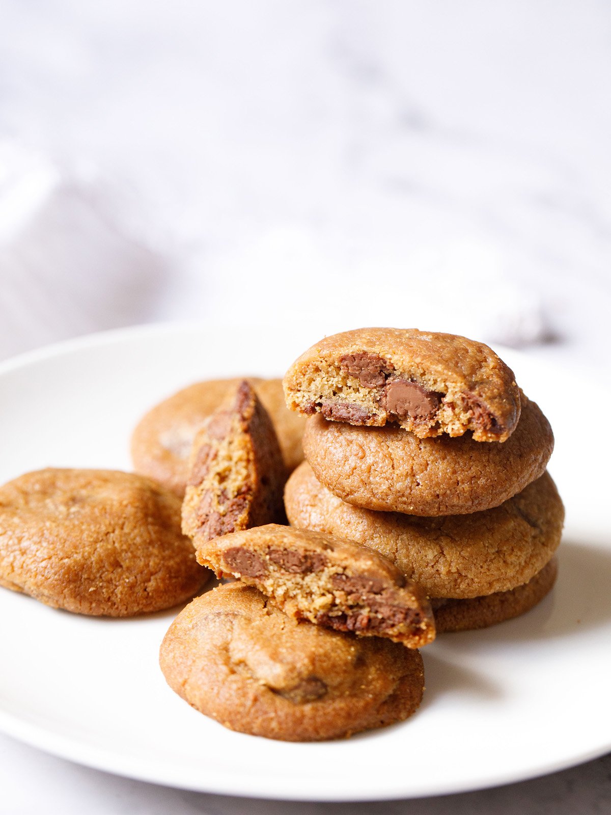 eggless chocolate chip cookies stacked with some halved cookies on a white plate