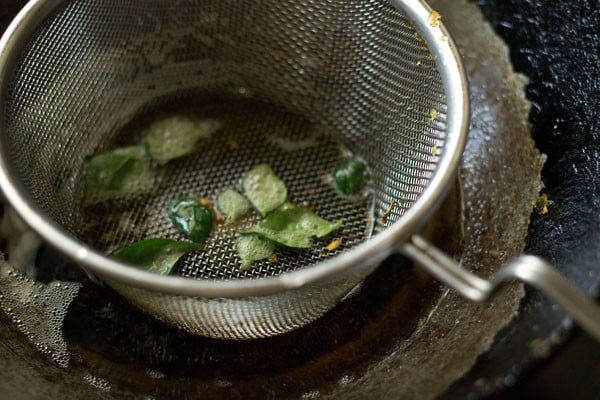 frying curry leaves in fine sieve ladle for making cornflakes chivda. 