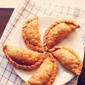 gujiya arranged neatly on a white plate placed on a white and blue checkered napkin p