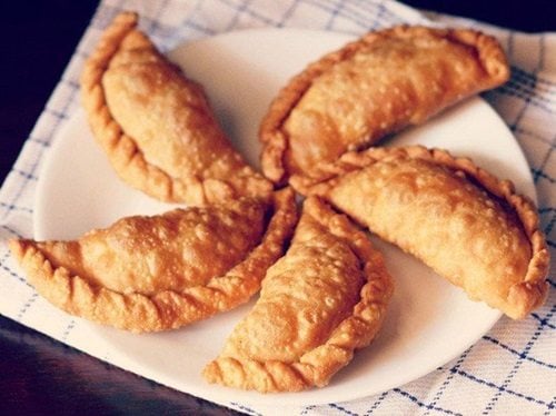 gujiya arranged neatly on a white plate placed on a white and blue checkered napkin