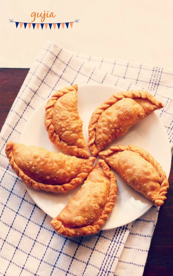 gujiya arranged neatly on a white plate placed on a white and blue checkered napkin p