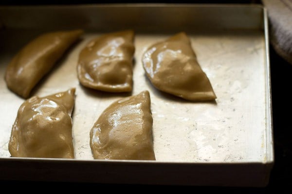 ghee brushed gujiya arranged on a baking tray