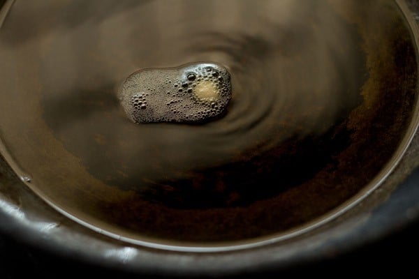 a small piece of dough sizzling in hot oil in a black work (kadai)