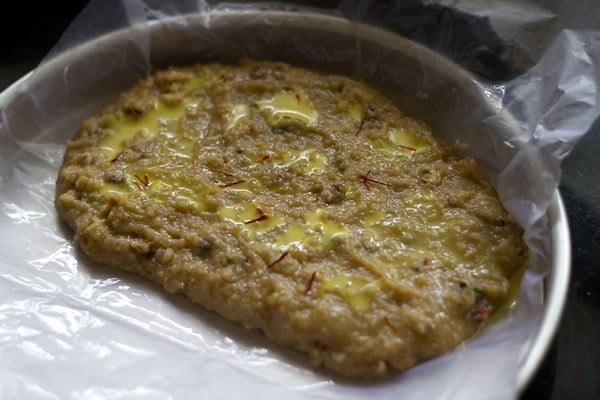 saffron milk added on the burfi mixture in the tray. 