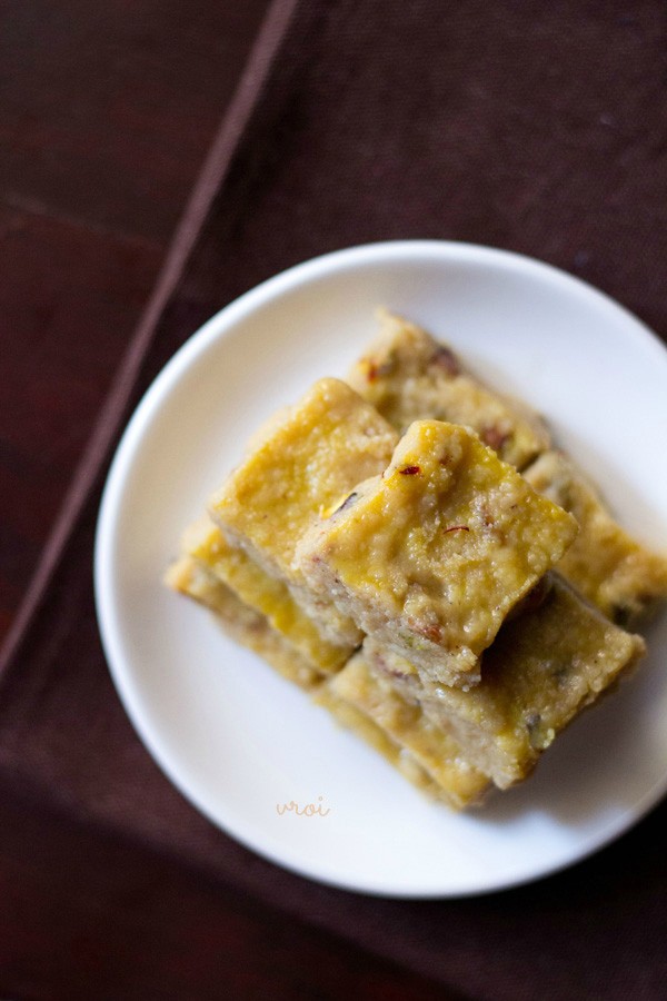 top shot of barfi squares stacked on top of one another and served on a white plate. 