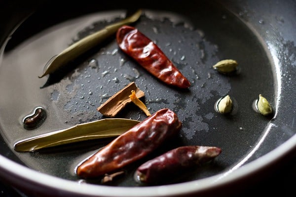 sautéing whole spices and dry red chilies in oil in a black frying pan