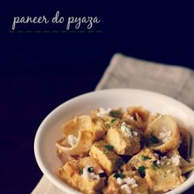 paneer do pyaza garnished with grated paneer and coriander leaves in a white bowl on a light beige napkin on a dark brown board