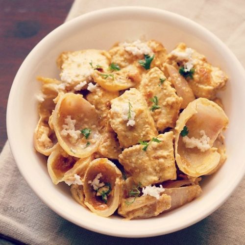 paneer do pyaza garnished with grated paneer and coriander leaves in a white bowl on a light beige napkin on a dark brown board