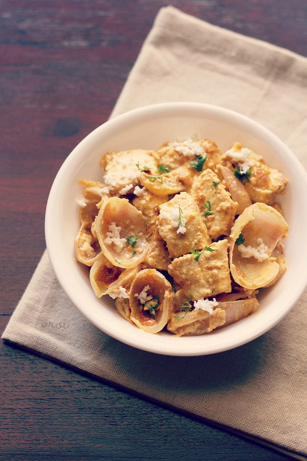 paneer do pyaza garnished with grated paneer and coriander leaves in a white bowl on a light beige napkin on a dark brown board