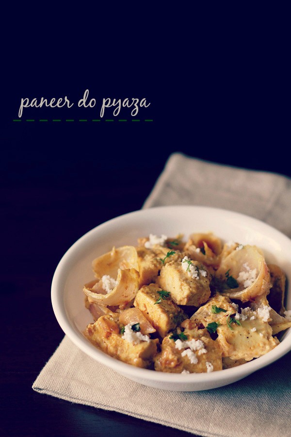 paneer do pyaza garnished with grated paneer and coriander leaves in a white bowl on a light beige napkin on a dark brown board