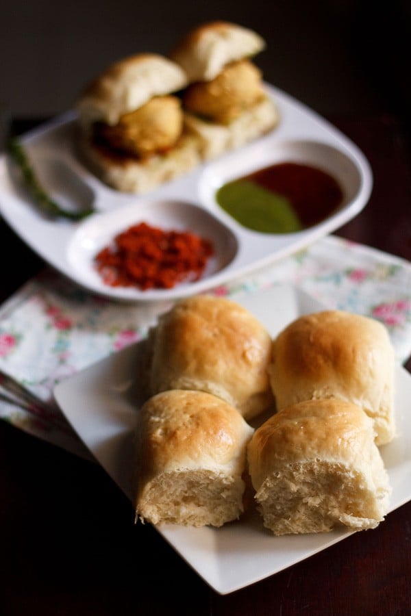 pav served with a plate of vada pav, garlic chutney, green chutney, tamarind chutney and fried green chili kept in the background. 