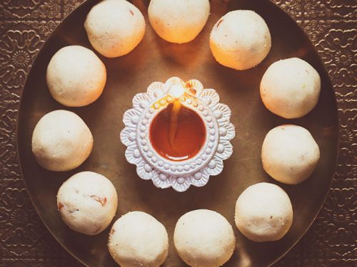 rava ladoo in a circle with lit earthern lamp in center on a bronze plate