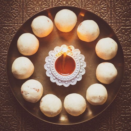 rava ladoo in a circle with lit earthern lamp in center on a bronze plate