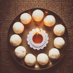 rava ladoo in a circle with lit earthern lamp in center on a bronze plate