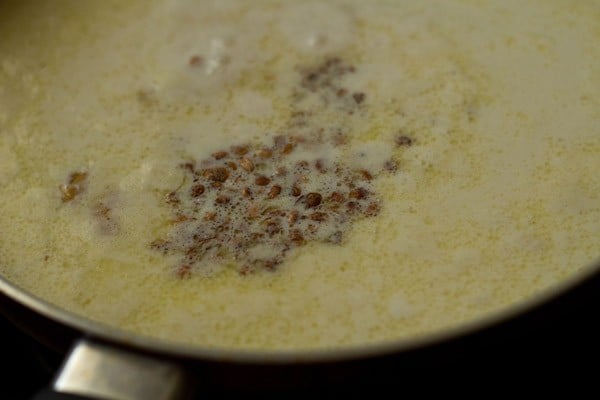 adding cardamom powder and nuts to suji kheer in pan