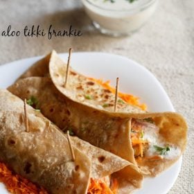 two rolled veg frankie on a bed of grated carrots on a square shaped white plate on a burlap