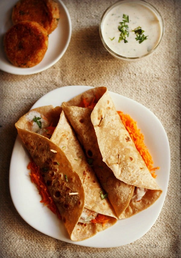 overhead shot two rolled frankie on a bed of grated carrots on a square shaped white plate on a burlap