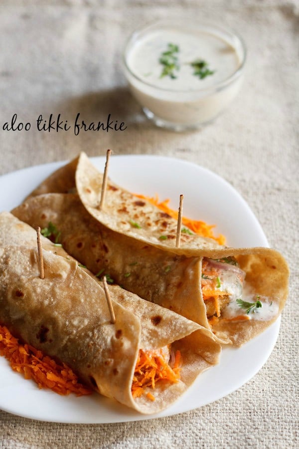 two rolled veg frankie on a bed of grated carrots on a square shaped white plate on a burlap