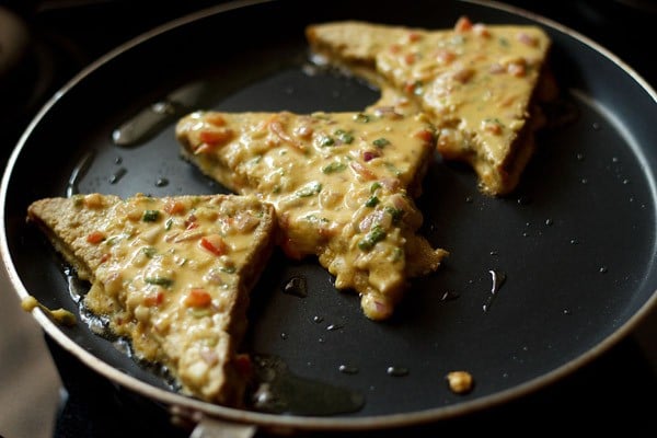 besan coated bread pieces placed on hot oil on tawa. 