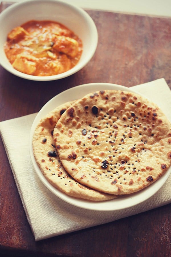 butter naan served on a white plate with a bowl of curry kept on the top left side. 